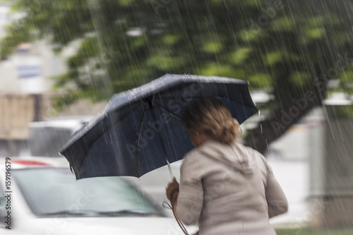 фотографія A woman is walking under the rain with her black umbrella