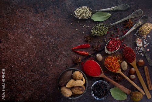Various indian spices in wooden and silver spoons and metal bowls, seeds, herbs and nuts on dark stone table. Colorful spices, top view, space for text. Organic food, healthy lifestyle.