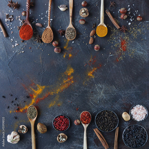 Various indian spices in wooden spoons and metal bowls, herbs and nuts on dark stone table. Colorful spices, top view,space for text. Healthy food background