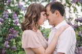 beautiful couple, the girl in beige light dress, the guy the white shirt, cuddling with their eyes closed, foreheads pressed against each other near the tree, greens, summer, lilac, close-up, nature