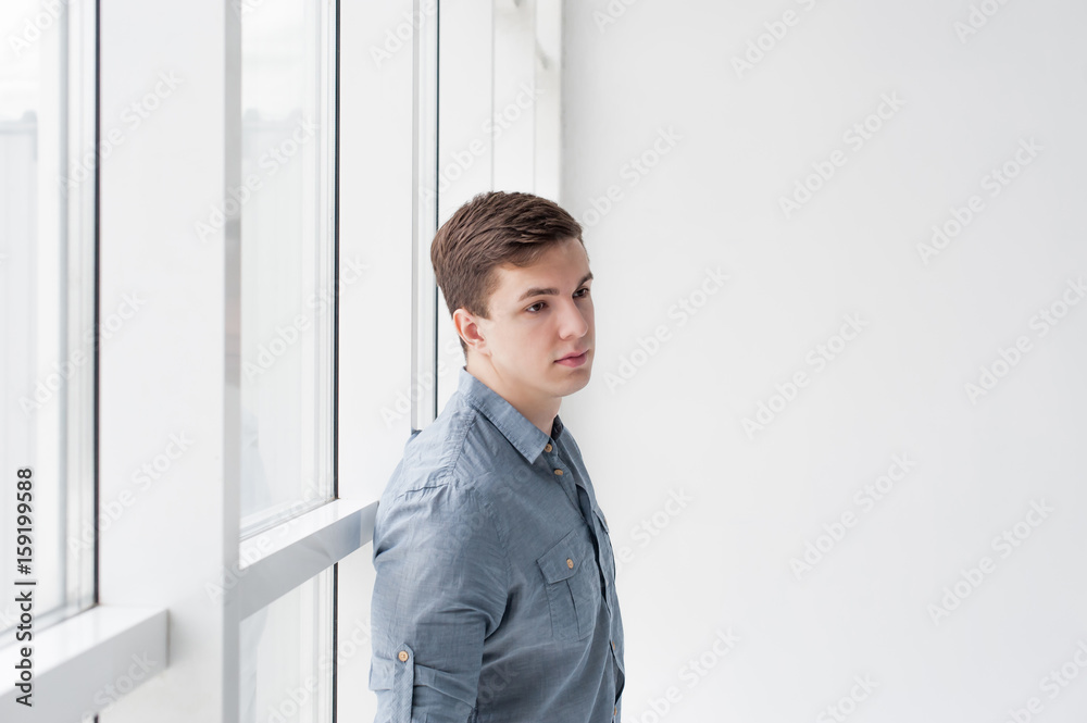 Young handsome man of strong athletic build, dressed in a shirt and brown trousers, Posing on white studio background, near window in full wall, hugging her back Young handsome man of strong athletic build, dressed in a shirt and brown trousers, Posing on white studio background, near window in full wall, hugging her back