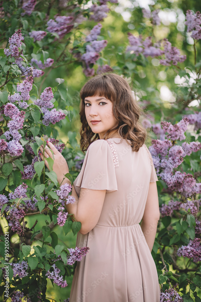 beautiful young sweet girl in a beige dress standing near a lilac tree with purple flowers back, profile, turned her face with a smile, summer, nature, forest, Park, walk, close-up