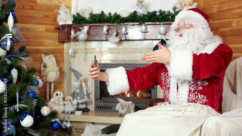 santa talking via skype, santa claus using gadget, decorated christmas tree, saint nicolas sending merry kisses by videocall, christmas preparation, room with fireplace, using digital device for volte