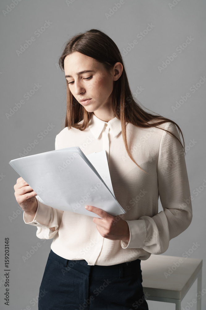 Businesswoman holds the papers in her hands and reads what is written there. Isolated on gray background. Businesswoman holds the papers in her hands and reads what is written there. Isolated on gray background.