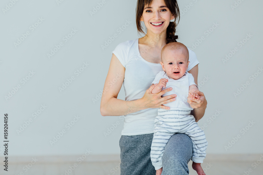 Athletic young smiling woman in sports dress doing fitness exercise with little baby boy on her knee. Mother having fun and working out with her little son. Athletic young smiling woman in sports dress doing fitness exercise with little baby boy on her knee. Mother having fun and working out with her little son.