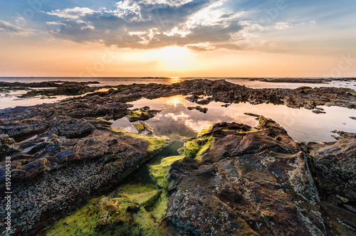 Beautiful seascape. Sunset over the sea rock and shore. A thin orange line at the horizon and the blue sky background and moss on rock foreground with the sunlight reflection on the water - wide angle