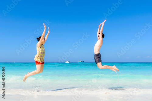 The happy Cheerful couple enjoys relaxing and jumping at white sand beach with blue sky and blue sea background.