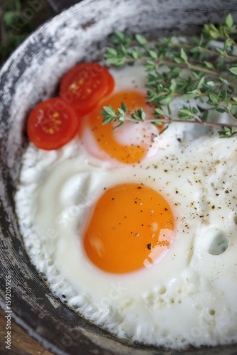Fried eggs in an old pan with tomatoes, pepper and thyme on a wooden table, Selective focus
