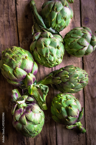 Bunch of ripe fresh colorful organic artichokes scattered on weathered wood table, rustic style, top view, atmospheric