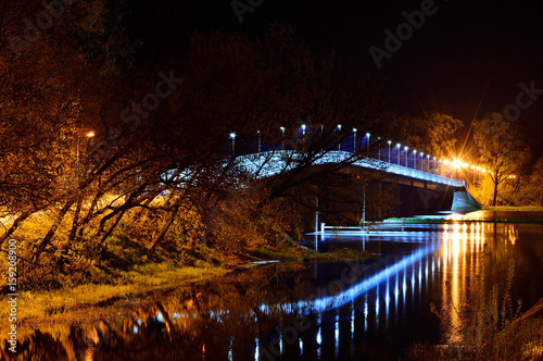 Most nad rzeka w nocy oświetlony latarniami. 