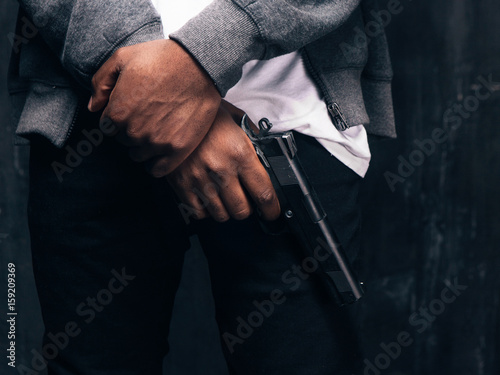 Unrecognizable armed black gangstercloseup studio shoot. Criminal man with gun in hand on dark background. Outlaw  ghetto  murderer  robbery concept
