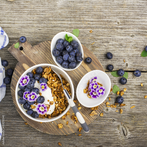 Healthy Breakfast: homemade roasted granola with blueberries, kiwi fruit and edible flowers on wooden background. From the top view. The concept of fitness nutrition
