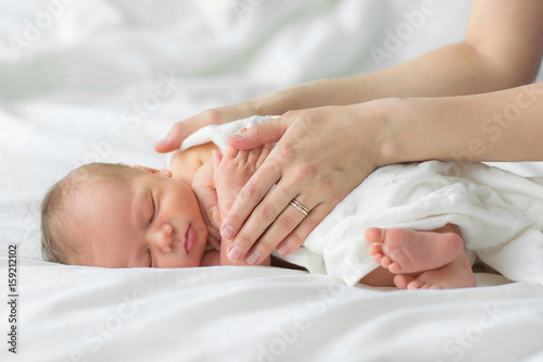 Newborn baby sleeping on a blanket. Mother gently strokes her child's hand