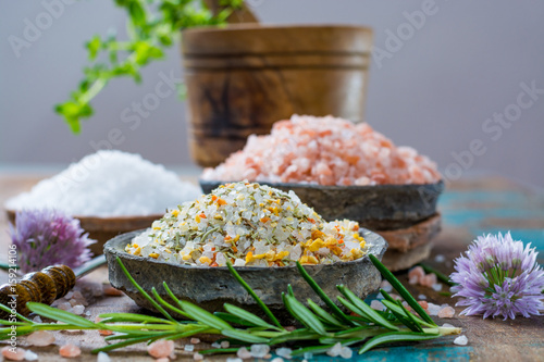 Three different types of natural salt in stone bowls on wooden surface. White sea salt, pink Himalayan salt, Spiced salt with rosemary photo