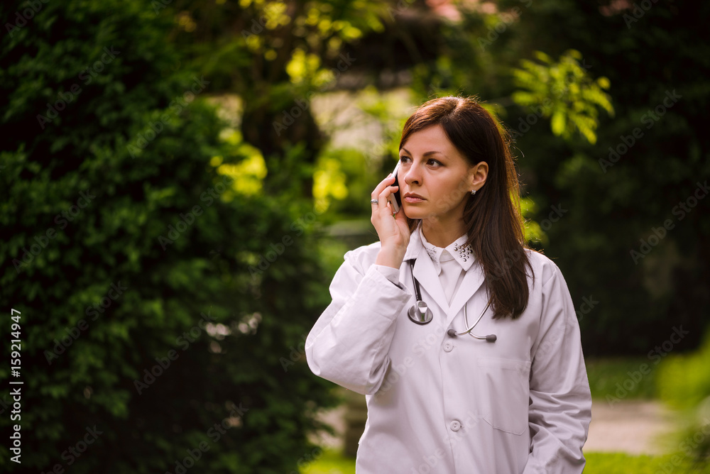 Female doctor talking on mobile over a green trees background Female doctor talking on mobile over a green trees background