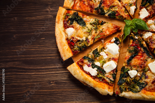 Pizza with feta cheese and spinach on wooden table