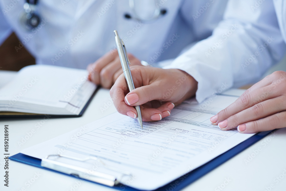 Female doctor filling medical form while consulting patient Female doctor filling medical form while consulting patient