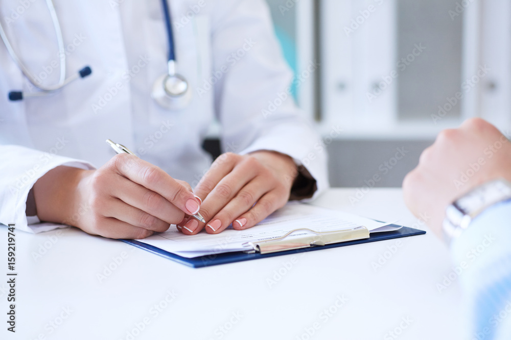 Female doctor filling medical form while consulting patient Female doctor filling medical form while consulting patient