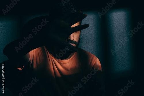 Konstfotografi Prisoner man in dark cell hiding face with shame