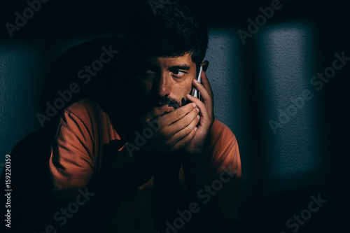 Prisoner man in dark cell using cell phone discreetly
