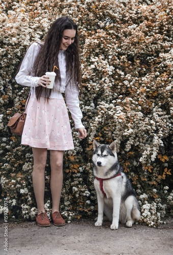 Girl in pink dress with a hussy dog on a background of flowering bushes
