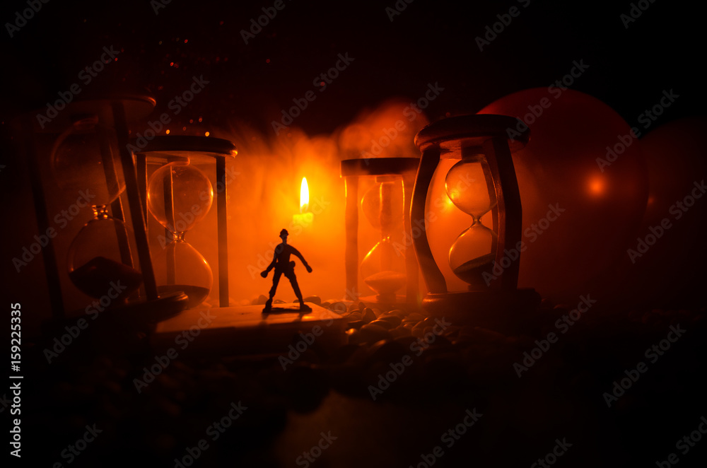 Time concept. Silhouette of a man standing between hourglasses with smoke and lights on a dark background.