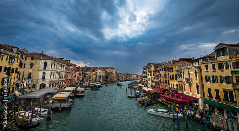 Panoramic view on famous Grand Canal among historic houses in Venice, Italy at dark, cloudy day with dramatic sky. Picture took from the Rialto bridge.