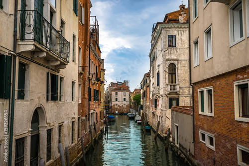 Panoramic view on famous Grand Canal among historic houses in Venice, Italy at cloudy day with dramatic sky, wood bridge and sitting woman on the foreground.