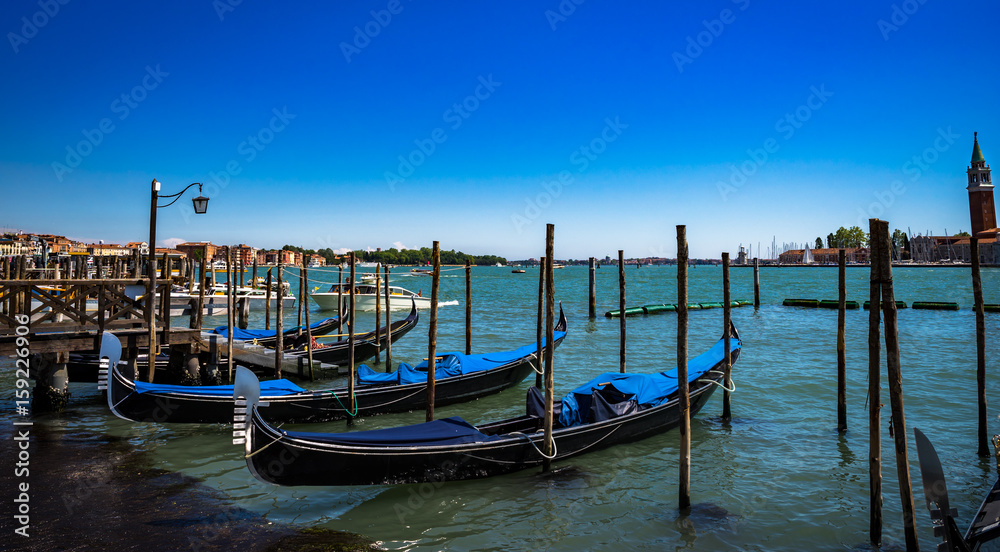 Gondolas moored by Saint Mark square with San Giorgio di Maggiore church on the background in Venice, Italy at sunny day.