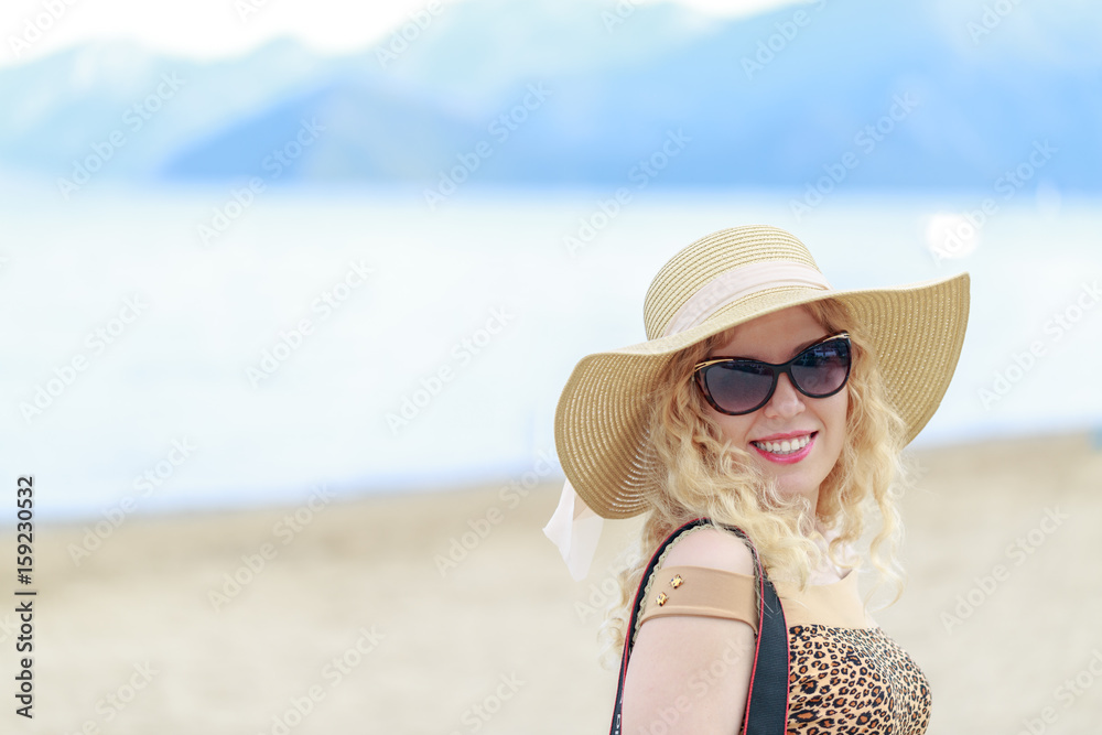 Beautiful blonde on the beach with hat and sunglasses in vacation