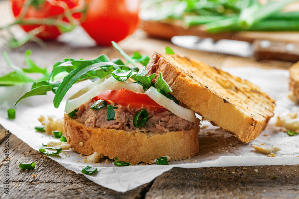 Grilled sandwich with tuna salad, tomato, onion and arugula on a wooden table. Diet healthy finger food made of toasts, vegetables and fish. Grilled sandwich with tuna salad, tomato, onion and arugula on a wooden table. Diet healthy finger food made of toasts, vegetables and fish.