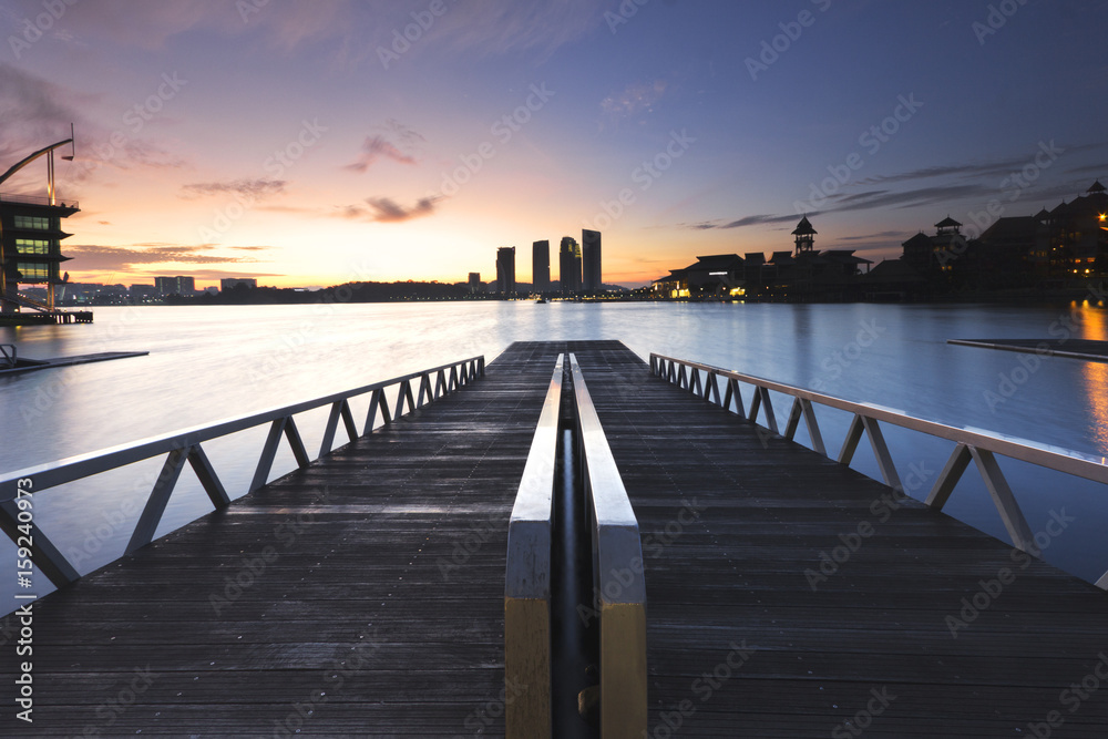A pier made of wooden and steel. Overlooking city during sunrise.