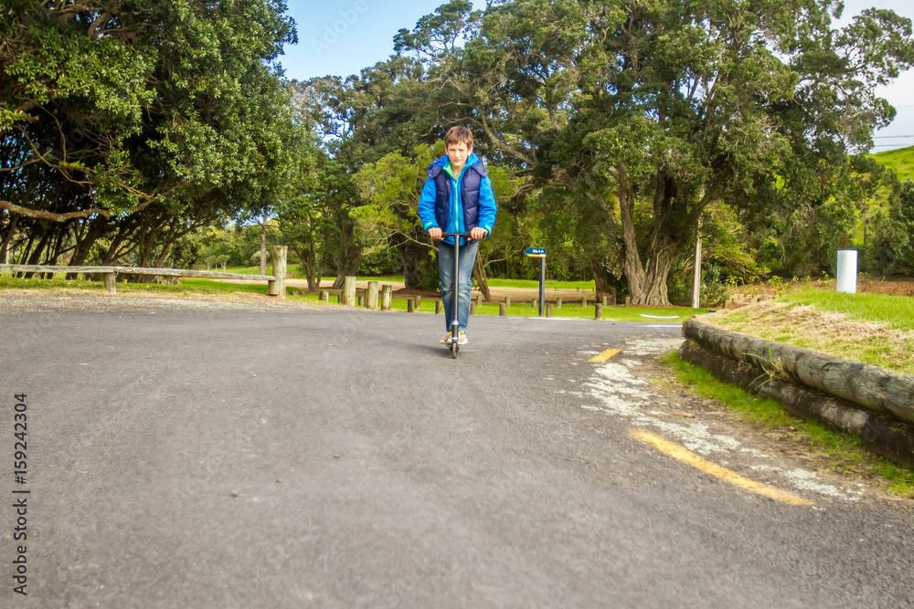 outdoor portrait of young happy preteen boy riding a scooter on natural background