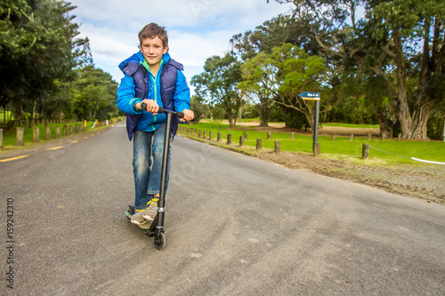 outdoor portrait of young happy preteen boy riding a scooter on natural background