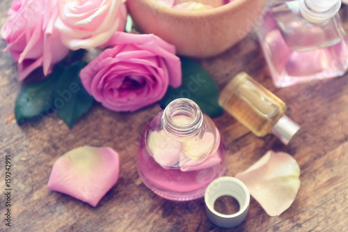 Essential oils with rose petals on wooden background