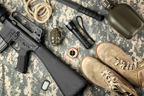 Set of military equipment and combat boots on camouflage background