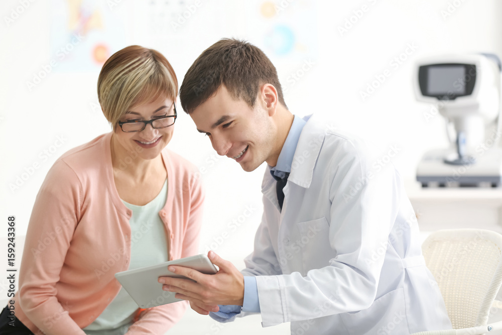 Young ophthalmologist with tablet computer and mature patient in clinic Young ophthalmologist with tablet computer and mature patient in clinic