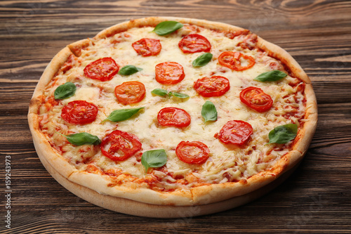 Delicious pizza with tomatoes, basil and melted cheese on wooden background