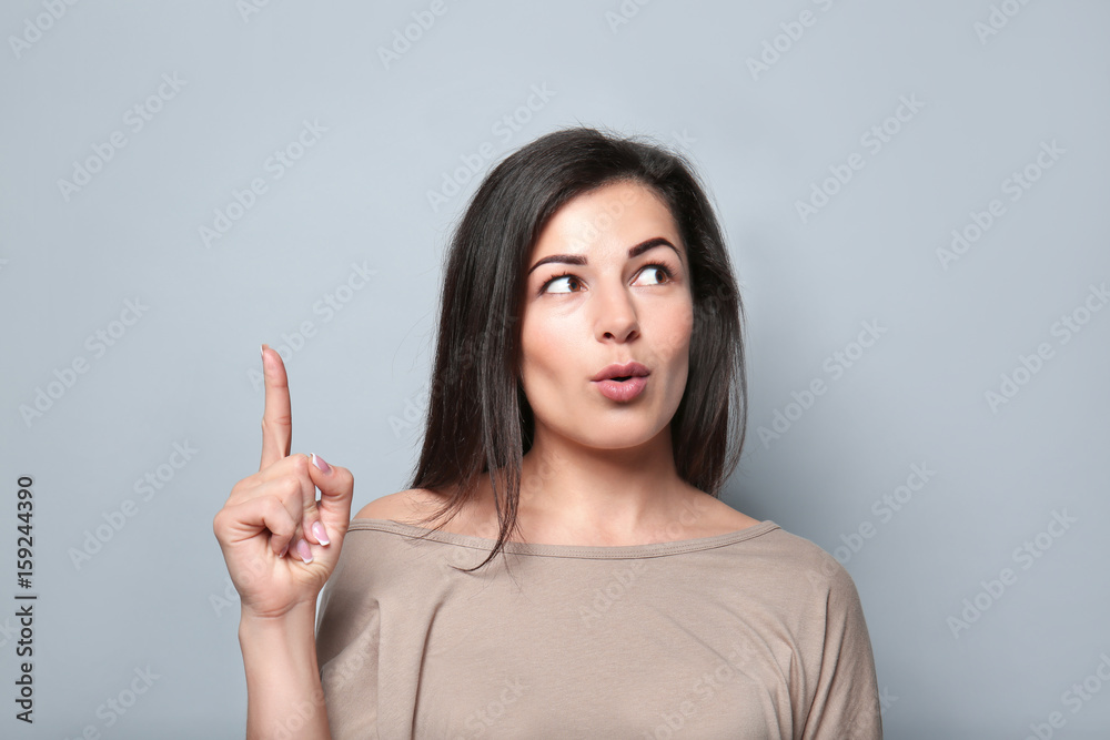 Portrait of young woman pointing with finger on grey background Portrait of young woman pointing with finger on grey background