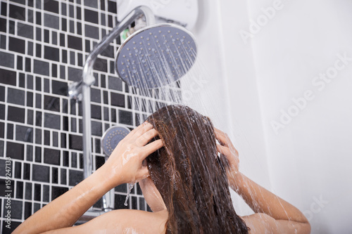woman is washing her hair and face by rain shower, rear view