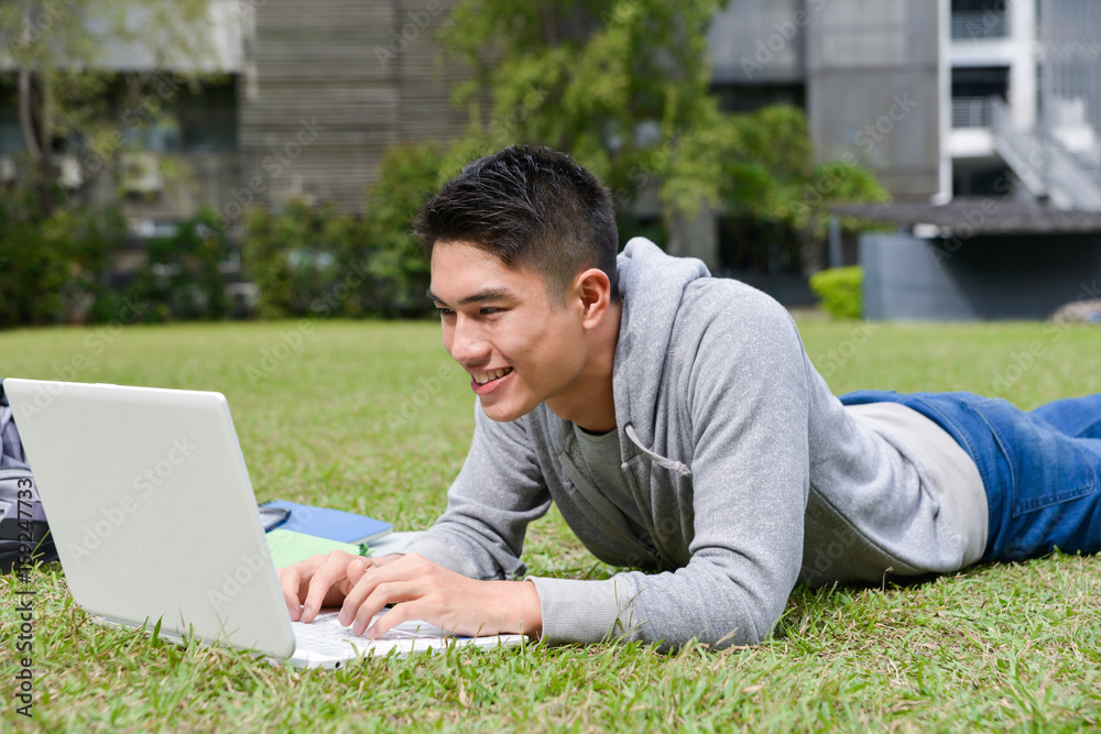 asian male college student lying on use laptop on a campus
asian male college student lying on use laptop on a campus