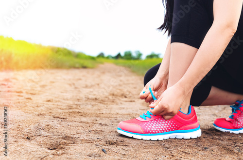 Female runner tying her running shoes on a sandy trail
