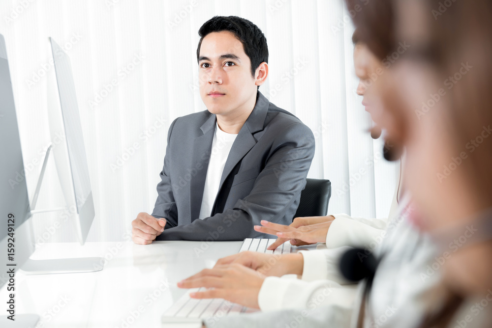 Young businessman  as a manager (or supervisor) sitting beside staffs in call center