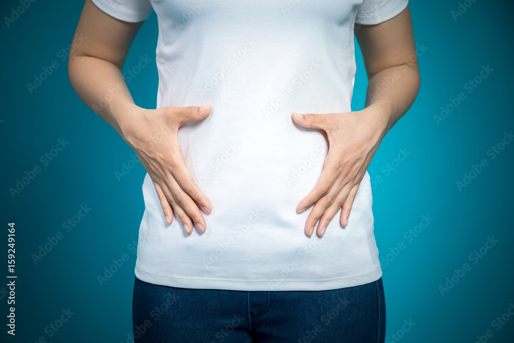 Young woman hand holding her stomach on a blue background Young woman hand holding her stomach on a blue background