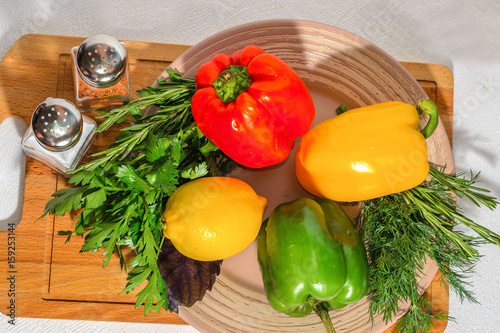 Fresh bright vegetables  Bulgarian pepper  herbs  lemon  on a ceramic plate  on a wooden cutting board