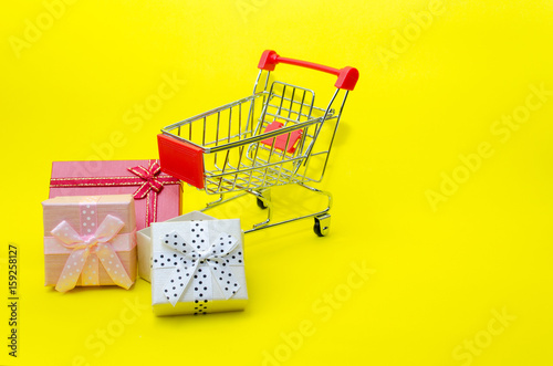 mini colorful gifts box in mini supermarket shopping cart on yellow background, holiday sale and online shopping concept, selective focus, copy space