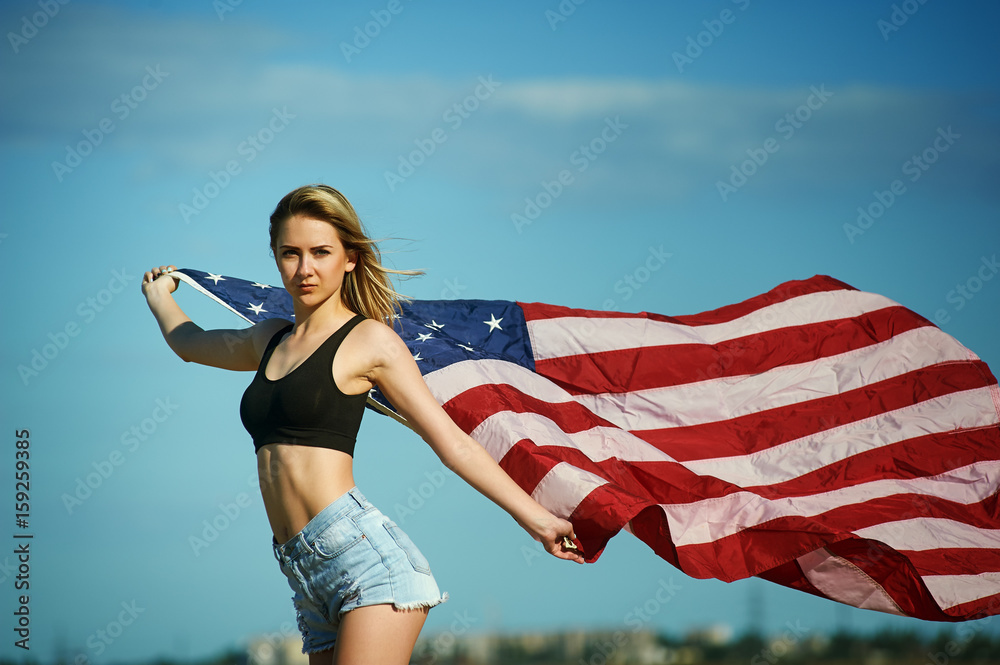 Girl with waving U.S. flag on blue sky background .