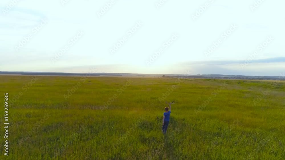 Happy child playing with a toy airplane against the background of an orange sun against a background of green grass. Happy child playing with a toy airplane against the background of an orange sun against a background of green grass.