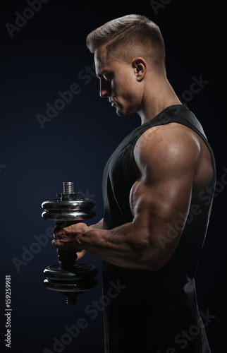Handsome power athletic man in training pumping up muscles with dumbbell. Strong bodybuilder with perfect deltoid muscles, shoulders, biceps, triceps and chest. Close-up of a power fitness man.