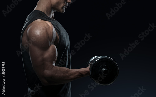 Handsome power athletic man in training pumping up muscles with dumbbell. Strong bodybuilder with perfect deltoid muscles, shoulders, biceps, triceps and chest. Close-up of a power fitness man.